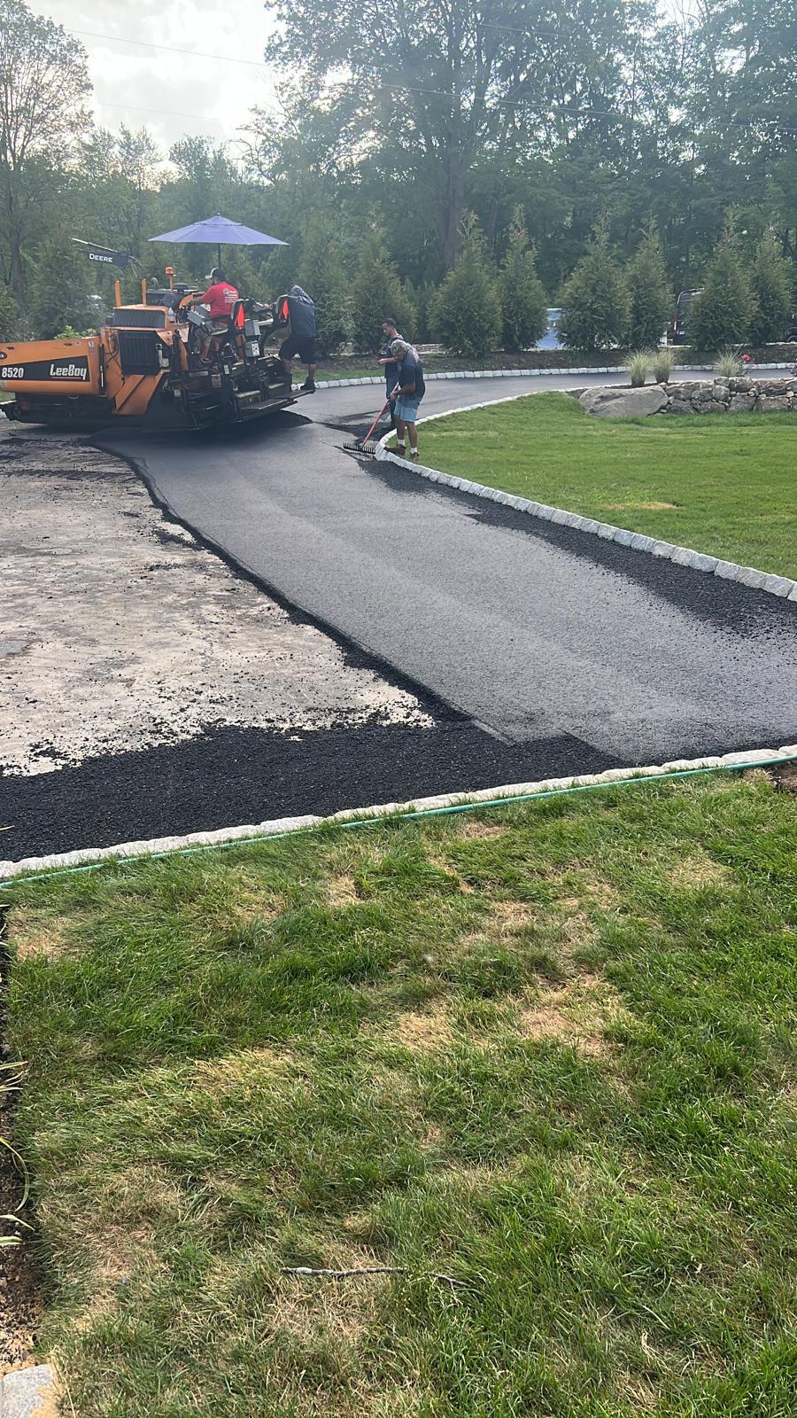 Construction workers using a paving machine to lay fresh asphalt on a residential driveway