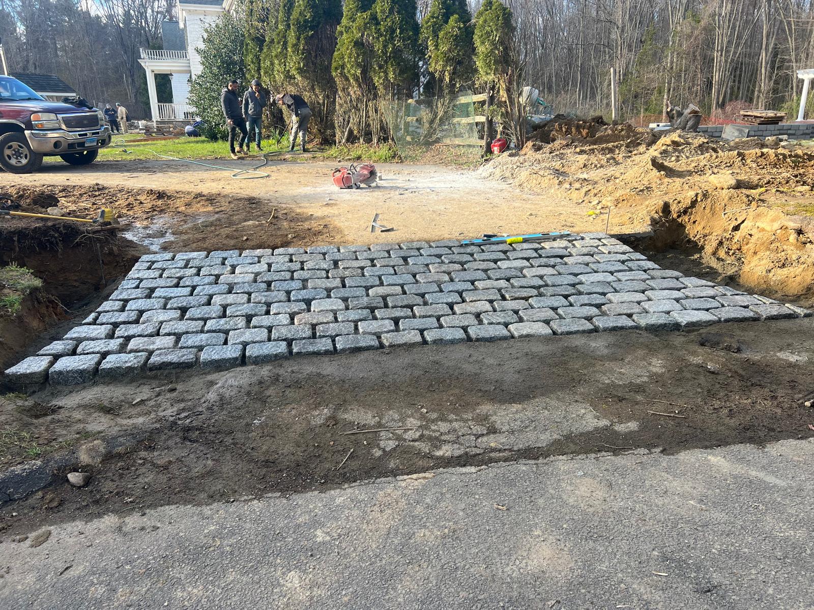 Newly laid gray cobblestone section in a dirt driveway at a construction site.