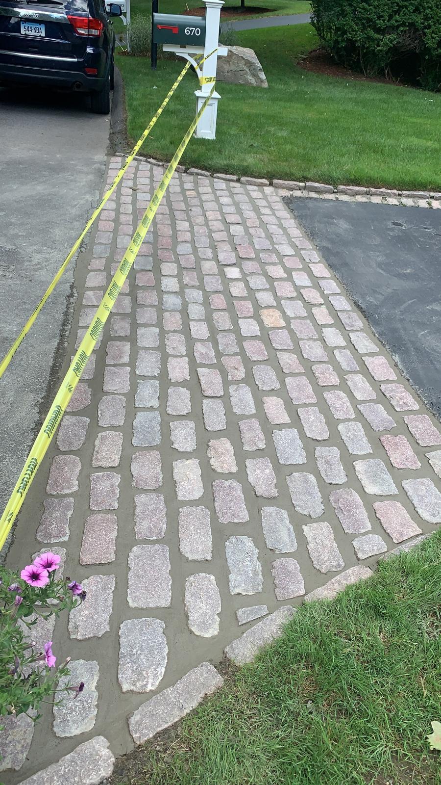 A newly installed cobblestone apron with wet mortar, cordoned off by yellow caution tape.