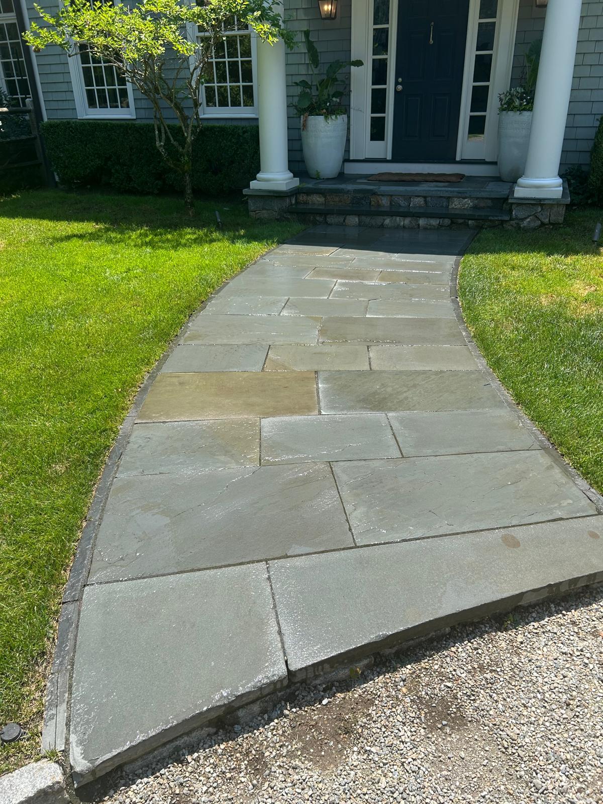 A flagstone walkway leading to the front door of a house with green lawns.